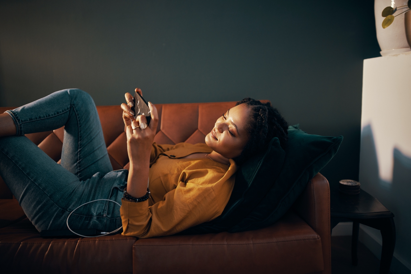Woman laying on a brown couch in her living room, holding her Galaxy smartphone in landscape mode and she looks at the mobile gaming screen. Woman laying on a brown couch in her living room, holding her Galaxy smartphone in landscape mode and she looks at the mobile gaming screen.