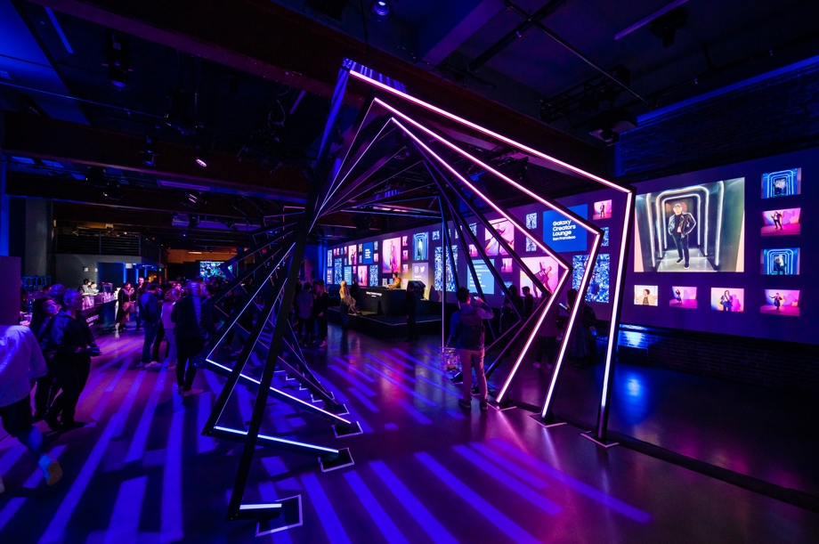 A wide shot of influencers gathered in the Creators Lounge event space. You can see a colorful light installation in the front and a DJ stage and bar in back.