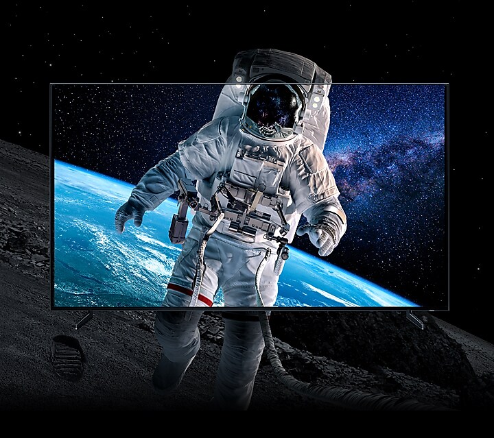 Closeup shot of an astronaut on the surface of the Moon, with footprints visible in the dirt. The image bleeds outside of a QLED 8K screen demonstrating how realistic the images are on this top of the line screen.