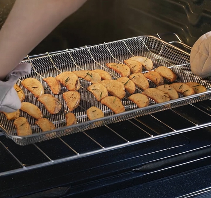 Healthier cooking⁴ with a crunch Hands Grabbing an Air Fry Oven Tray Filled with Rosemary Roasted Potato Wedges