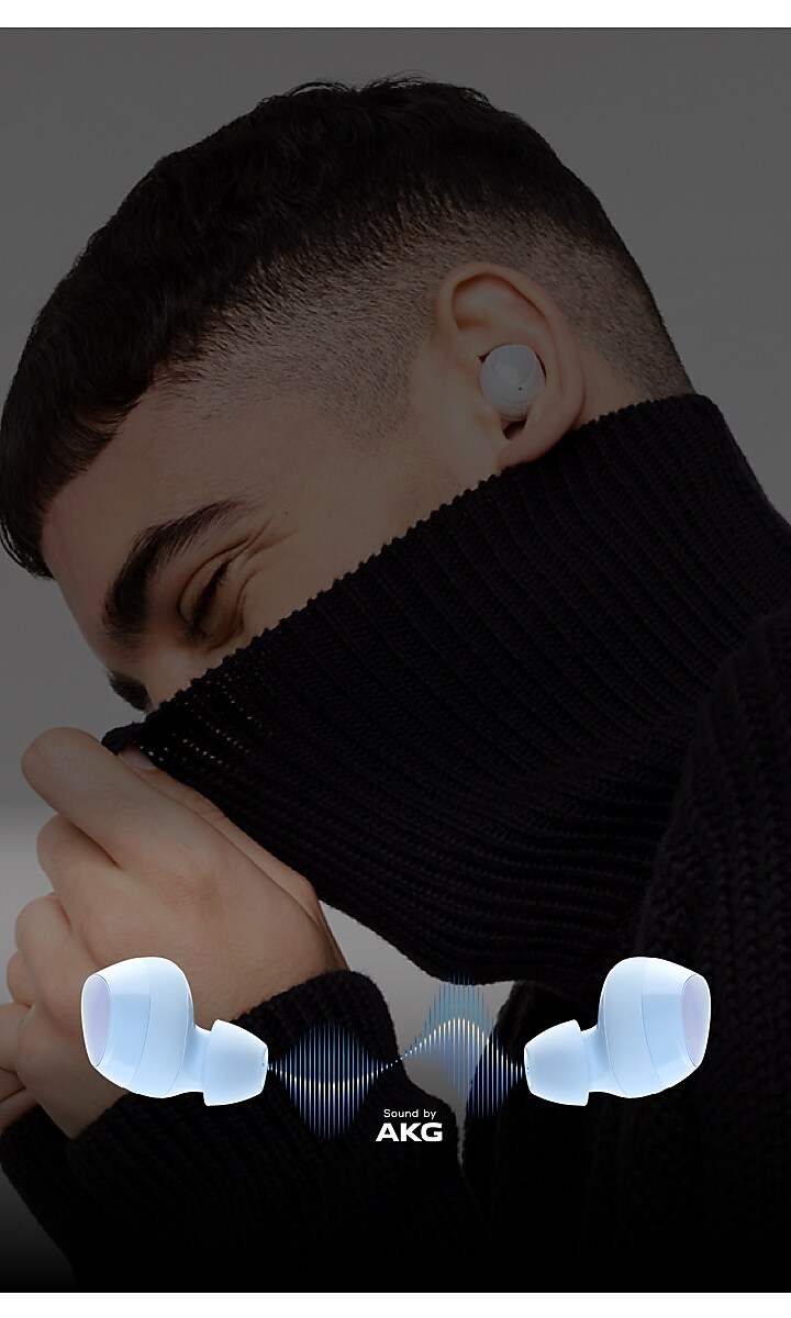A man with a closely cropped hair is seen from the side wearing the buds in his left ear. He is also pulling up a turtleneck sweater playfully above his nose. Below him is an image of the buds tilted outward with a blue sign wave graphic between them along with the text "Sound by AKG" A man with a closely cropped hair is seen from the side wearing the buds in his left ear. He is also pulling up a turtleneck sweater playfully above his nose. Below him is an image of the buds tilted outward with a blue sign wave graphic between them along with the text "Sound by AKG"