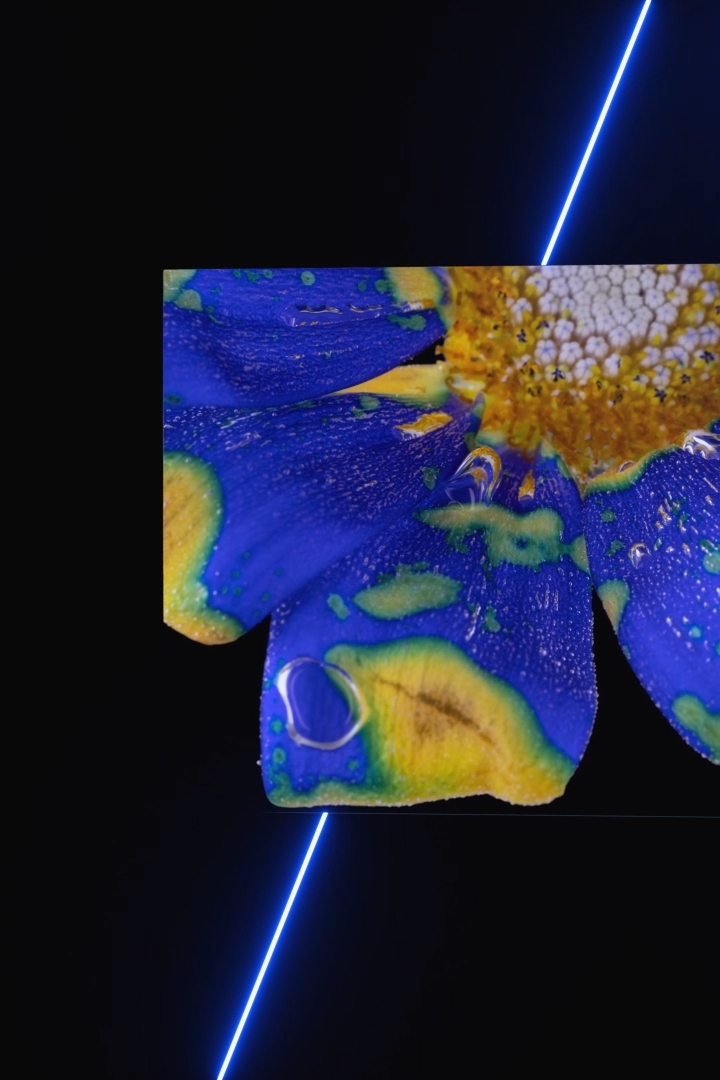 A QLED TV begins with a full front view of the QLED TV as it sits positioned in a darkly lit studio room. The on-screen simulated visual shows a combination of various blue, orange, and green colors moving and mixing with each other. Itbegins to switch between various angles which highlight the main features of the QLED TV including overall product appearance, rear speaker locations, and its slim bezel.