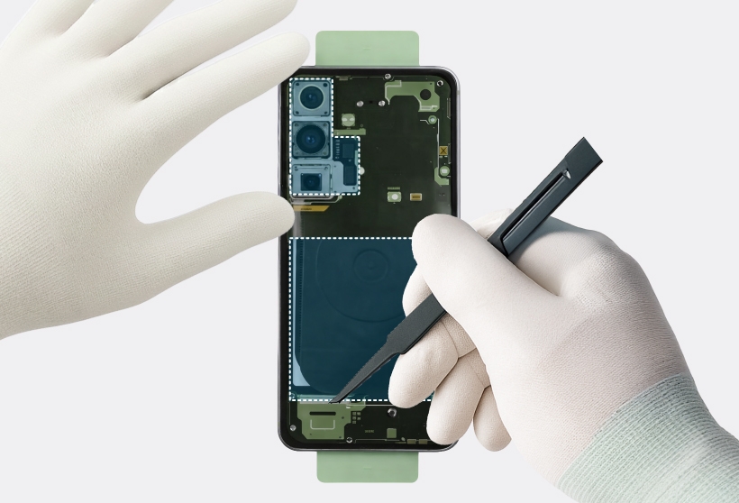 Gloved hands lifting the internal camera frame and wireless charging coil assembly from the Galaxy S25.