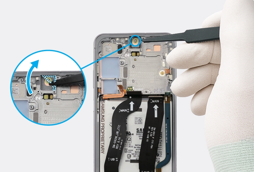 Gloved hand using tweezers removing the adhesive and tape from the front camera hole on the device.