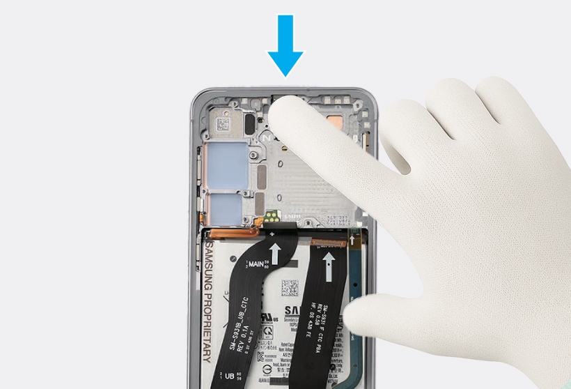 Gloved hand pressing down on the camera module with an index finger.