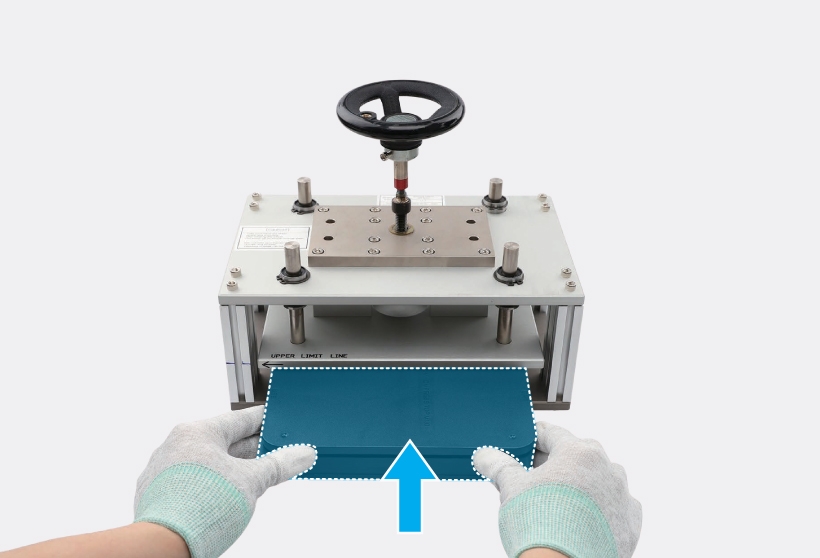 Gloved hands positioning the back cover press tray horizontally into the center of the press fixture, with a blue highlight indicating the press tray and a blue up arrow icon indicating the positioning direction.
