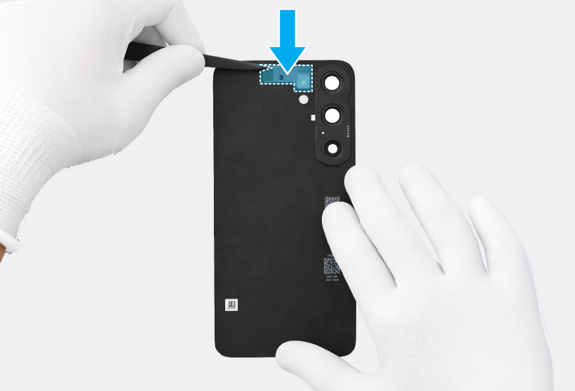 A gloved hand using tweezers attaching the microphone hole adhesive tape around the microphone hole on the inside of the back cover of a Galaxy S25 Plus, with a blue highlight with a blue down arrow icon indicating the adhesive area.