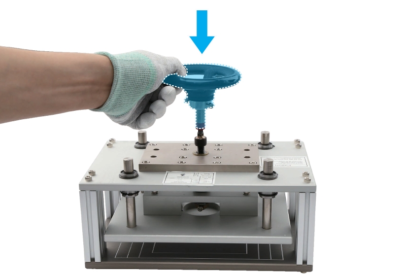 A gloved hand positioning the torque limit handle horizontally on the top of the press fixture, with a blue highlight indicating the torque limit handle and a blue down arrow icon indicating the positioning direction.