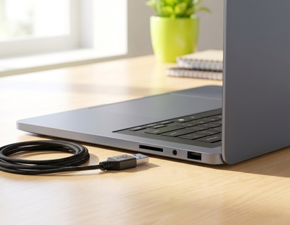 A laptop on a wooden desk next to a coiled USB cable.