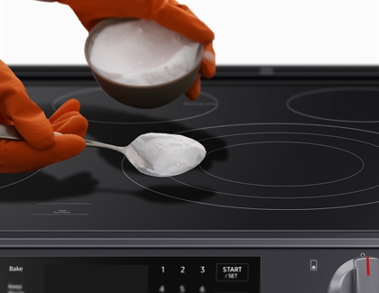 Person with orange gloves putting baking soda on Cooktop