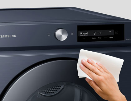 A hand cleaning the outside of a Samsung dryer.