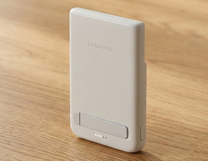 A gray Samsung battery pack standing on a wooden surface with four white LED lights illuminated at the bottom.