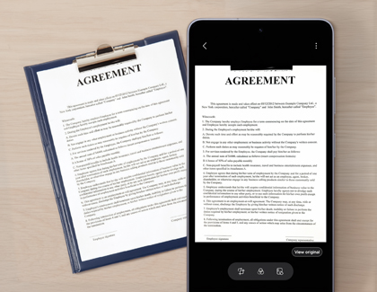 A Galaxy S26 Ultra on a wooden table next to a clipboard showing a scanned digital version of a paper agreement on its screen.