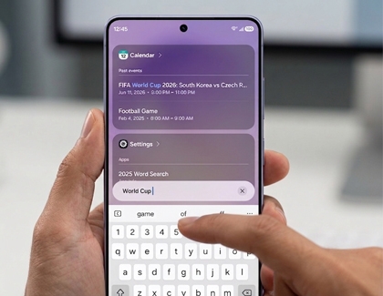 Hands holding a Galaxy S26 Ultra typing a search query into the Finder tool with calendar and settings results displayed above the keyboard.