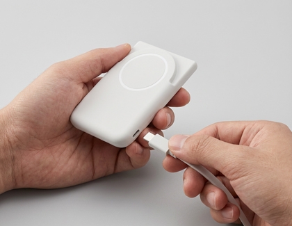 Hands holding a gray Samsung battery pack while connecting a white USB cable to the charging port.