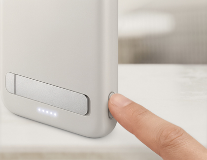 A finger pressing the side power button on a gray Samsung battery pack with five white LED lights lit up.