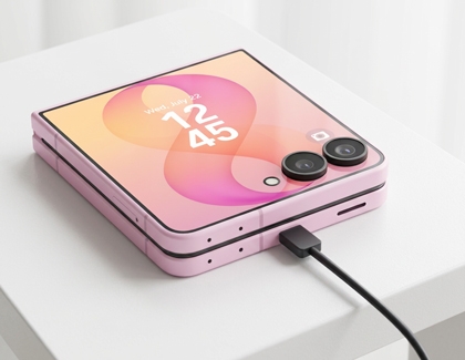 A pink Galaxy Z Flip8 displayed on a white surface showing the cover screen with a charger connected at the bottom.