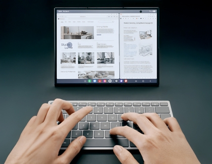 Unfolded internal screen of the Galaxy Z TriFold displaying two side by side browser windows behind a person typing on a gray wireless keyboard.