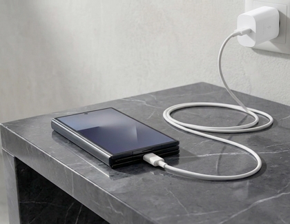 Folded Galaxy Z TriFold on a gray marble table connected to a white wall charger by a white cable.
