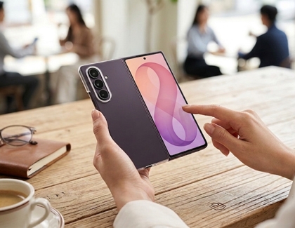 A person holding an open purple Galaxy Z Fold8 in a clear case at a wooden cafe table.