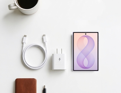 A purple Galaxy Z Fold8 Ultra lying next to a white USB-C wall charger, cable, wallet, and coffee cup on a light table.