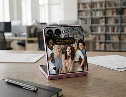 A pink Galaxy Z Flip8 standing partially folded on a desk displaying a group photo on the cover screen.