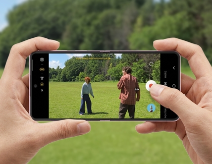 Hands holding a pink Galaxy Z Flip8 horizontally recording two people in a field.