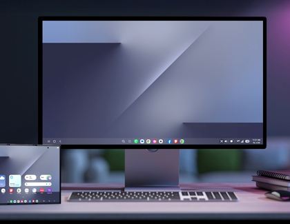 A monitor on a desk displaying the Samsung DeX desktop interface next to the Galaxy Z TriFold showing its home screen.