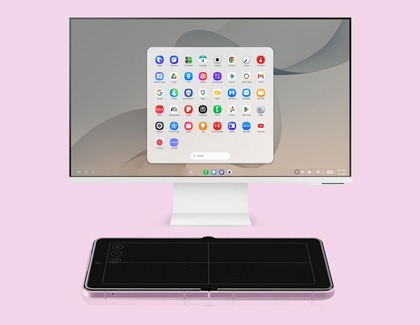 A computer monitor displaying Samsung DeX app grid with a pink folded Galaxy Z Fold phone lying flat in front acting as a touchpad.