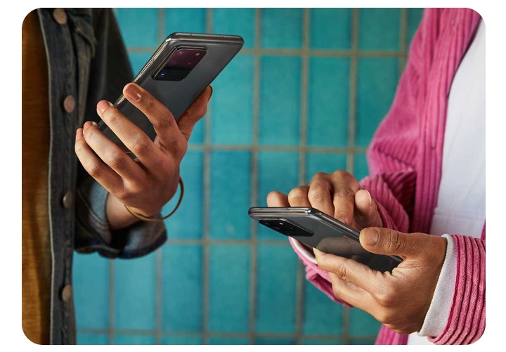 Close up shot of two people holding phones. The hand on the left is tiling the phone upward slightly while the other person is holding the phone and tapping it with the other hand. 