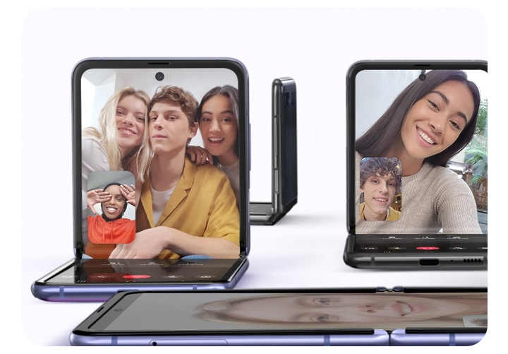The Galaxy Z Flip is positioned in four diffeent angles. One is facing the viewer and shows a video conference going on. Three people are in the screen while another is in the lower eft hand corner. Another phone is laying flat, one is the background while another is cut off on the right. 