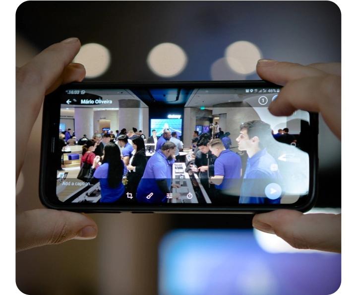 A close up of a Galaxy phone with the camera on. Through the screen, you can see the inside of a Galaxy Samsung Experience Store with workers helping people and phones out on display. A close up of a Galaxy phone with the camera on. Through the screen, you can see the inside of a Galaxy Samsung Experience Store with workers helping people and phones out on display.