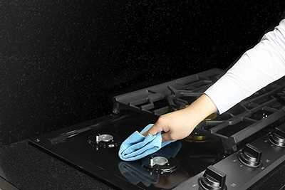 A hand wiping the cooktop surface with a cloth while the grate is removed