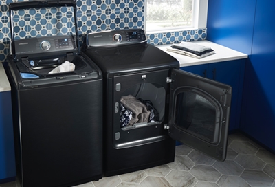 A Samsung dryer next to neatly folded white towels and a laundry basket