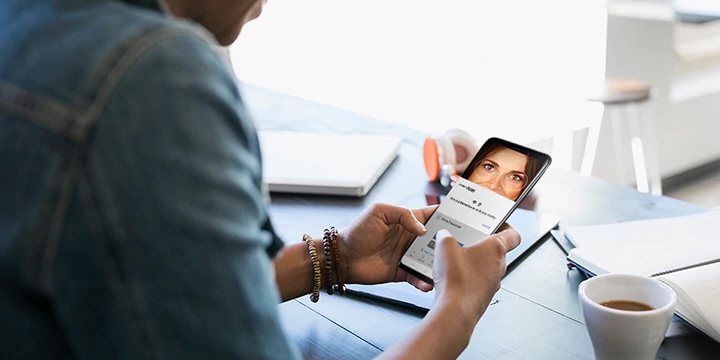 A woman at a café holding a smartphone in both hands using Samsung Pass to log in to an account.
