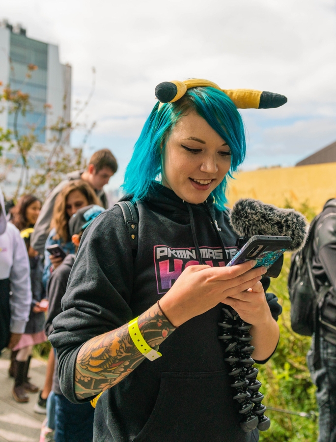 Holly Patterson stands and  smiles as she looks down  at her Galaxy Note10 phone in hand. She's surrounded by people who are walking next to her.