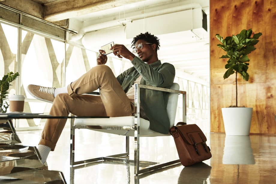 A casually-dressed man sitting at a station playing relaxing games on his Galaxy S10