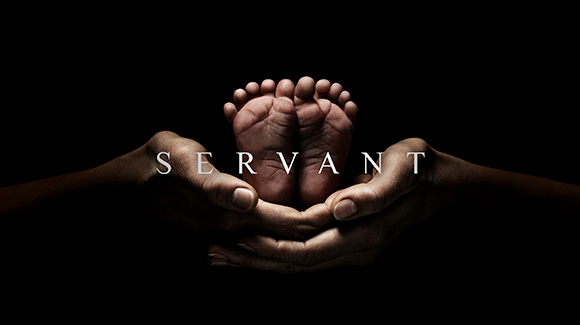 A promo shot for  the new Apple TV+ orginal show, Servant. The image is a pair of adult hands holding a pair of baby feet against a black background. The word "servant" is layered over the hands and feet.