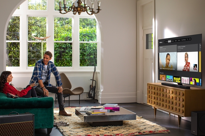 A man and a woman sit on a green couch in their living room deciding what to watch on TV.