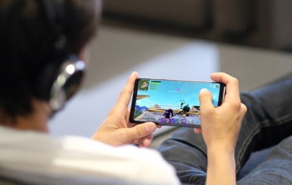 An over the shoulder shot of a man wearing headphones and playing Fortnite on the Samsung Galaxy Note9