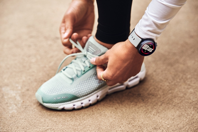 A below-the-shin shot of a lady tying her running shoe while wearing a Galaxy Watch Active2
