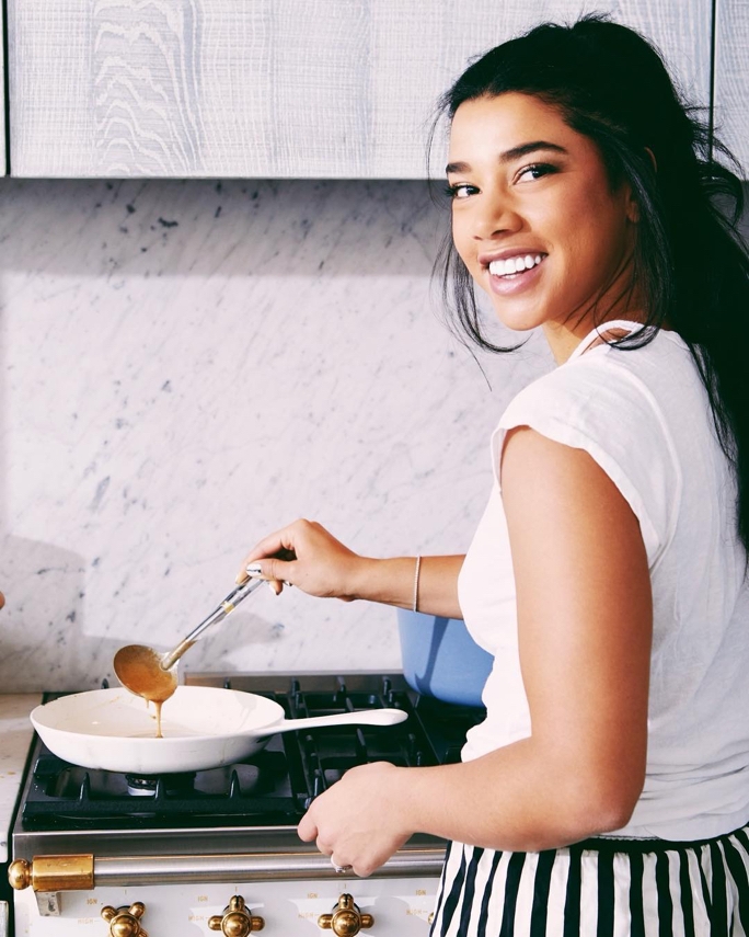 Hannah Bronfman in the kitchen cooking on the stove, she is smiling back at the camera
