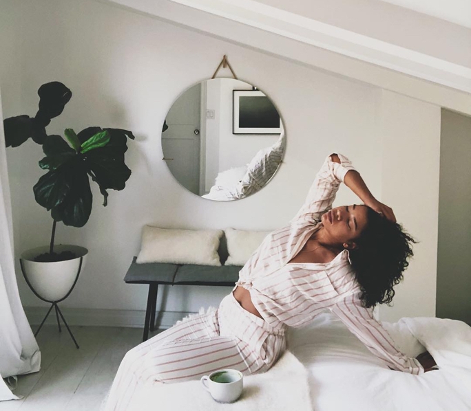 Hannah Bronfman in her bedroom stretching on her bed, there is a plant in the corner and a mug on the bed