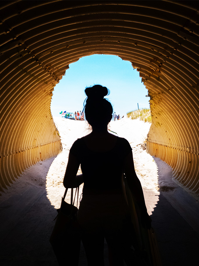 Woman walking through tunnel to beach.