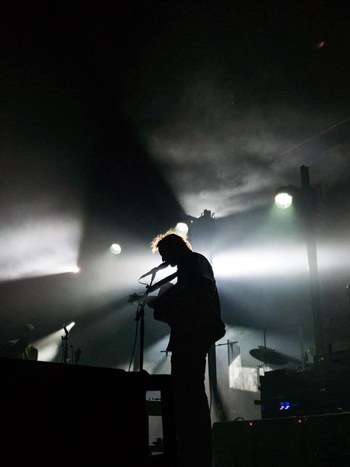 Man playing guitar on stage with white backlight.