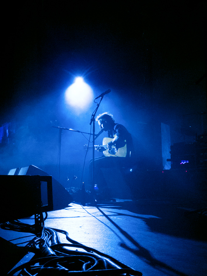 Man playing guitar on stage under blue light.