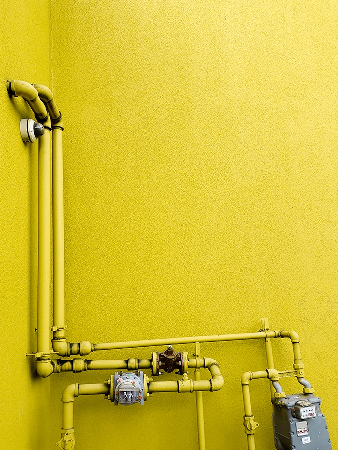 Pipes in front of yellow wall.