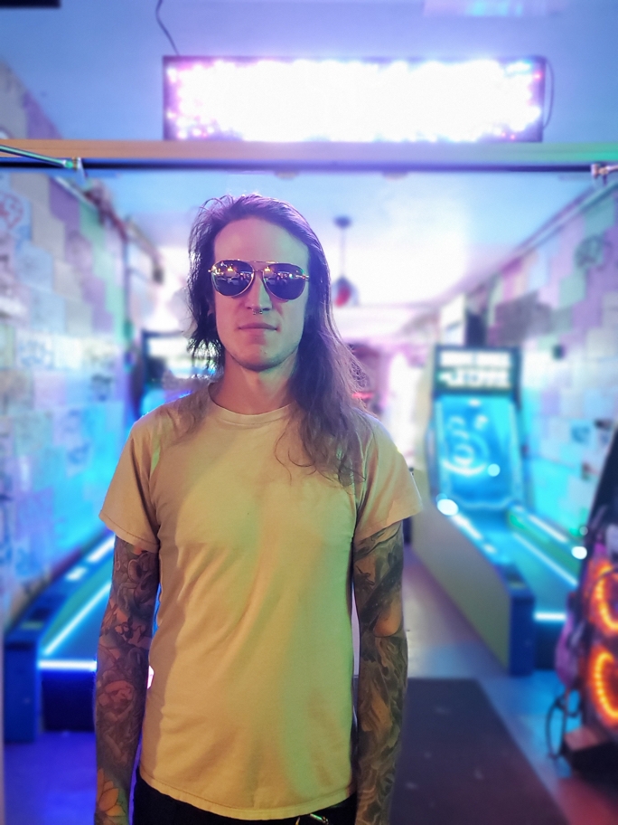 Man in sunglasses standing in front of a colorful and well-lit arcade
