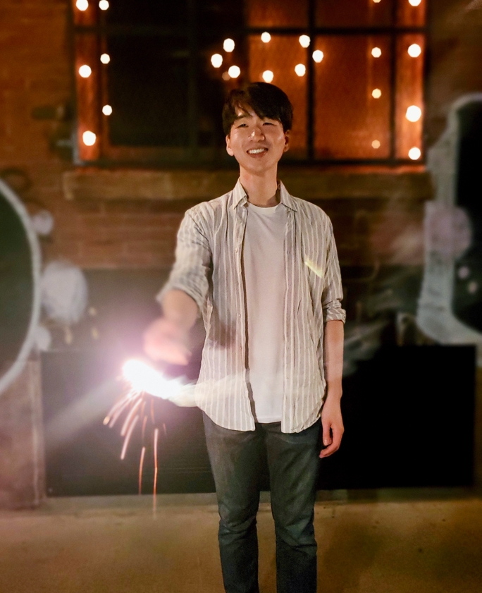 Man holding a sparkler while standing against a bokeh background covered in fairy lights