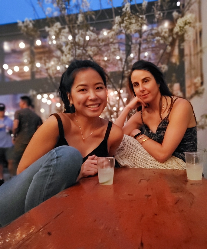 two women sitting at a table with fairy lights behind them